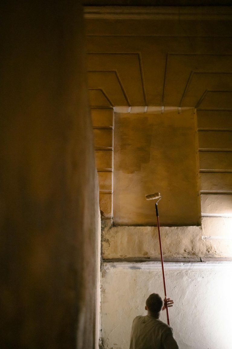 Man using a paint roller to update an indoor wall during renovation.